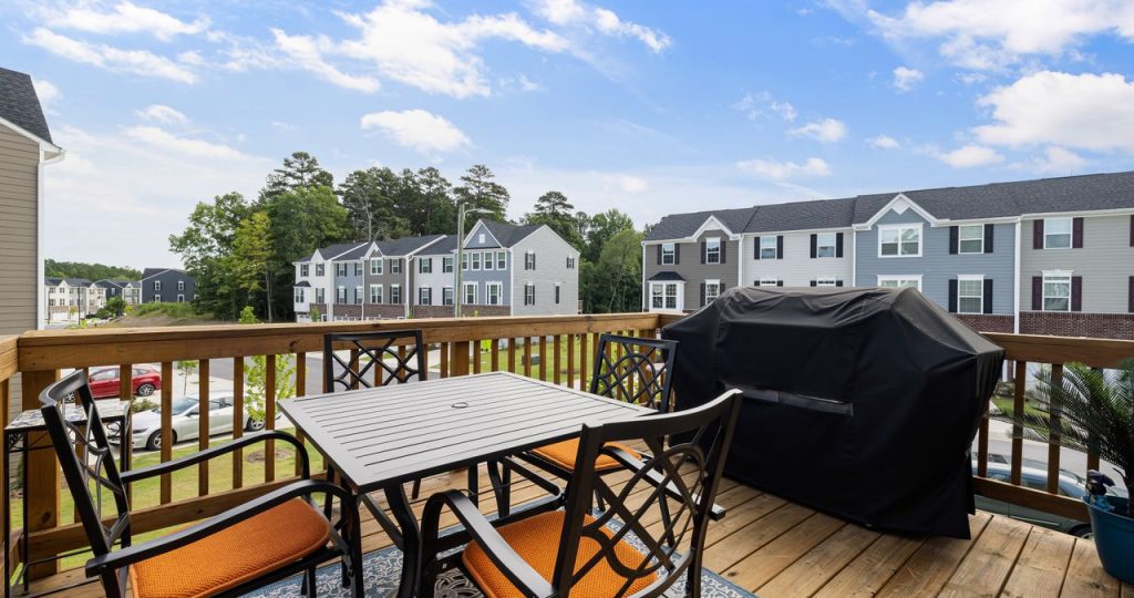 Charming wooden deck with furniture, grill, and suburban view.